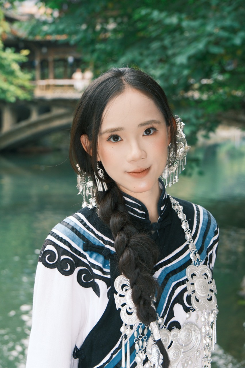 Chenshuo with a side braid beside a leafy waterway