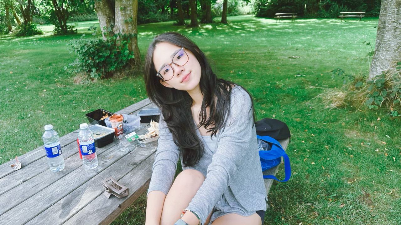 Chenshuo with glasses at a picnic table in a green park